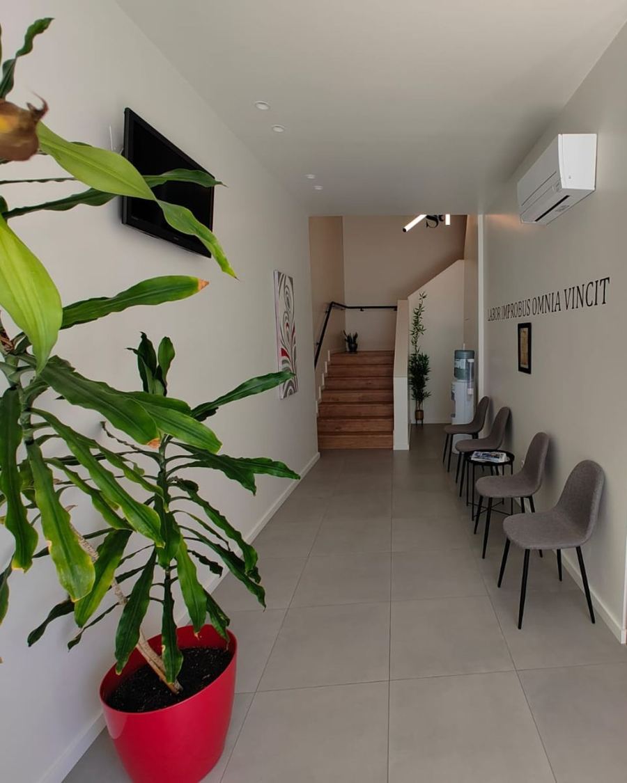 Corredor e zona de espera do escritório, com cadeiras, plantas e acesso ao piso superior
